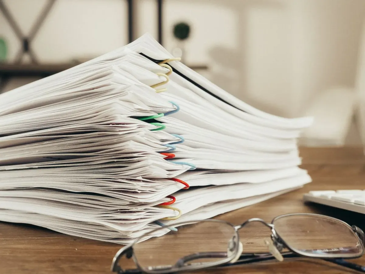 Stack of clipped documents and reading glasses on an office desk