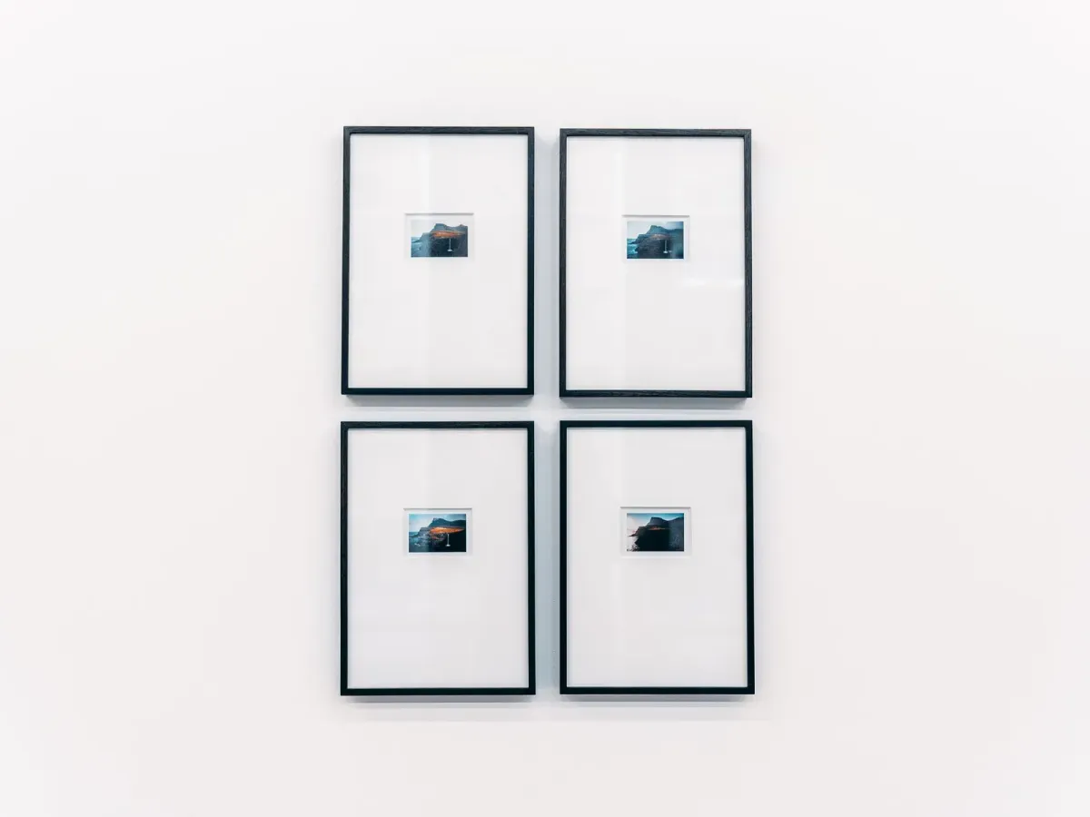 Four black frames holding small photographs on a white gallery wall