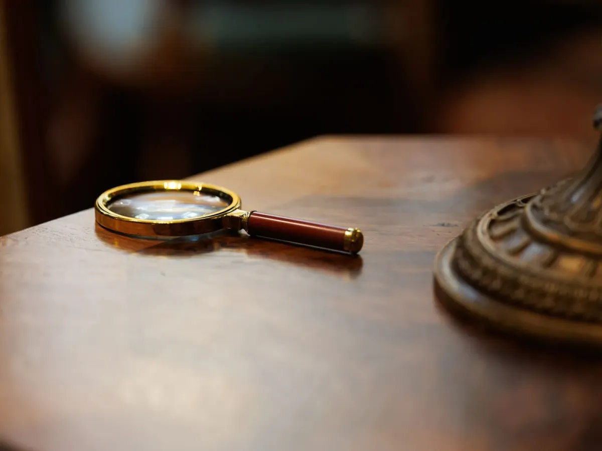 Une loupe posée sur une table en bois sombre, près du pied d’une lampe en laiton