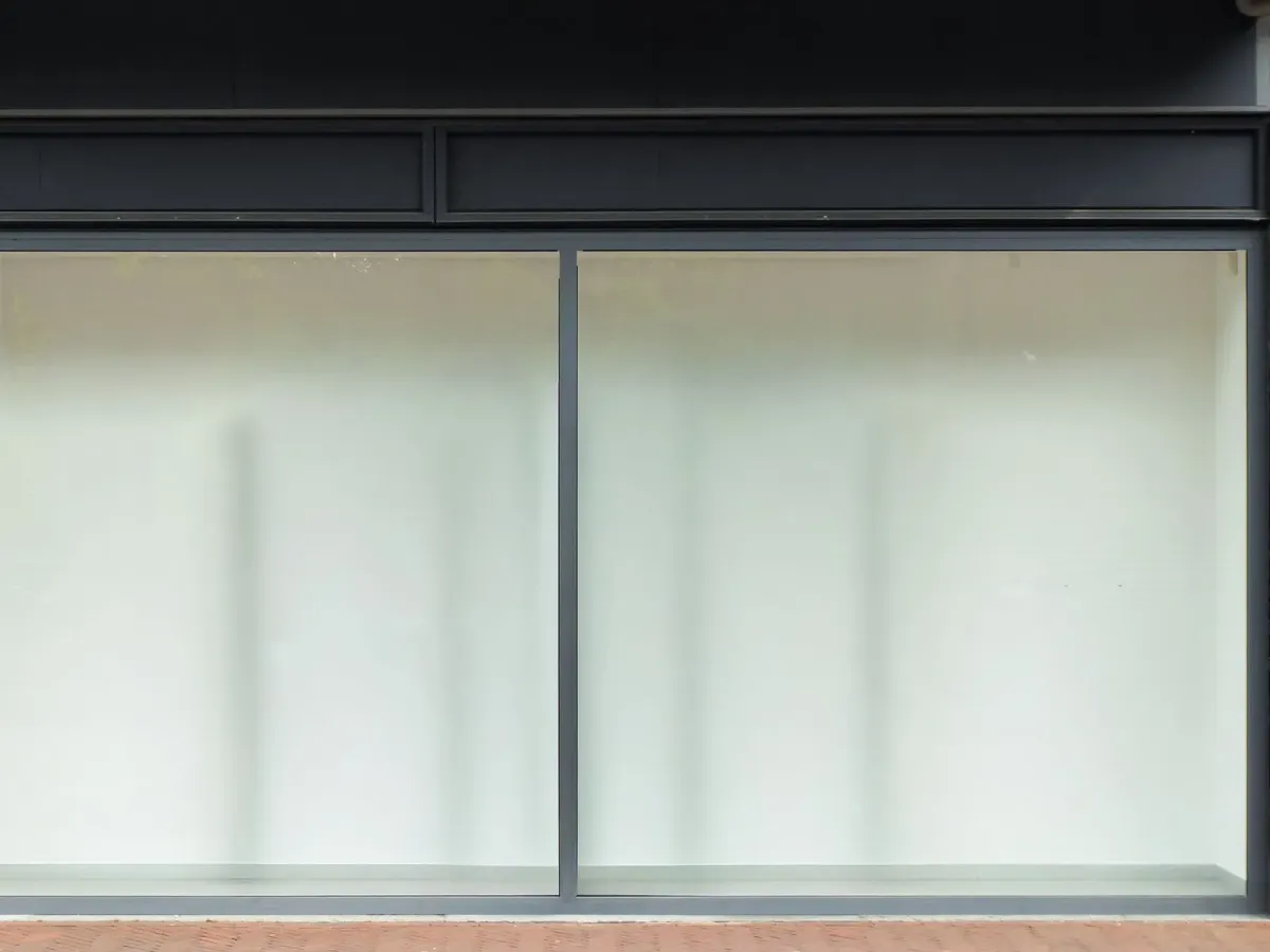 Vitrine vide d’un local commercial aux grandes baies, au bord d’un trottoir en briques