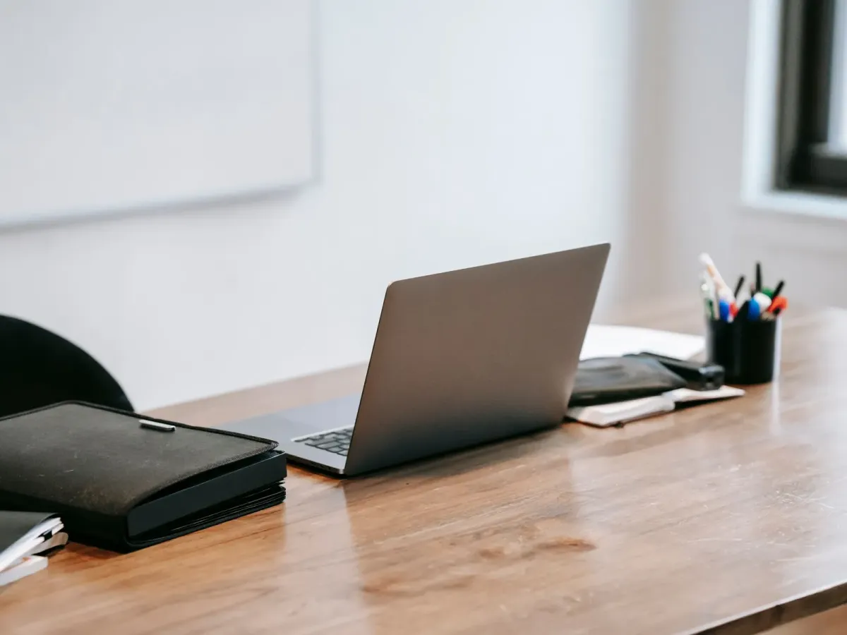 Ordinateur portable et pochette en cuir sur un bureau en bois, à la lumière du jour