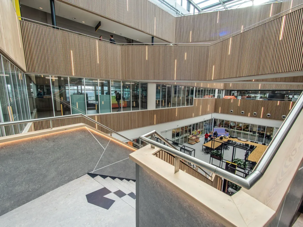 Atrium lumineux d’un immeuble de bureaux, avec un escalier et des galeries habillées de bois clair