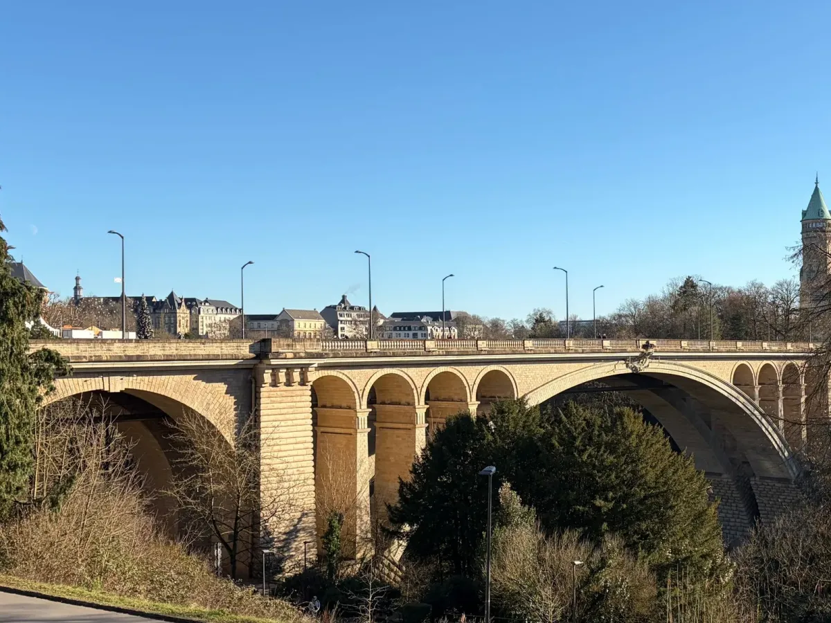 Le pont Adolphe à Luxembourg sous un ciel bleu, entre les arbres de la vallée de la Pétrusse