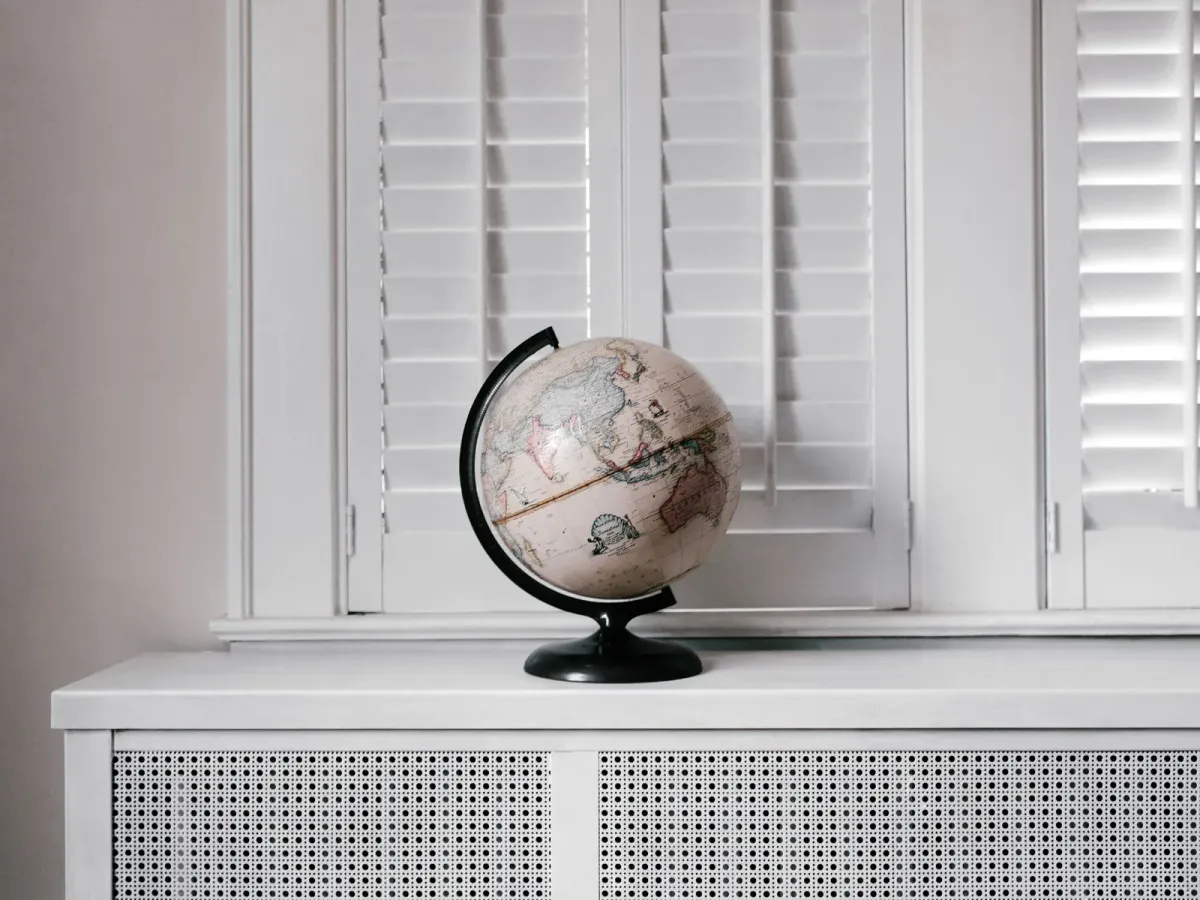 A desk globe on a white radiator cover in front of louvred window shutters
