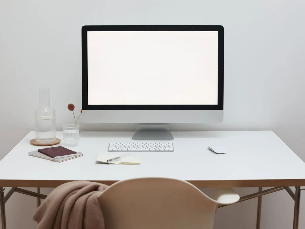 A tidy white desk with a computer, a notebook and a pale chair