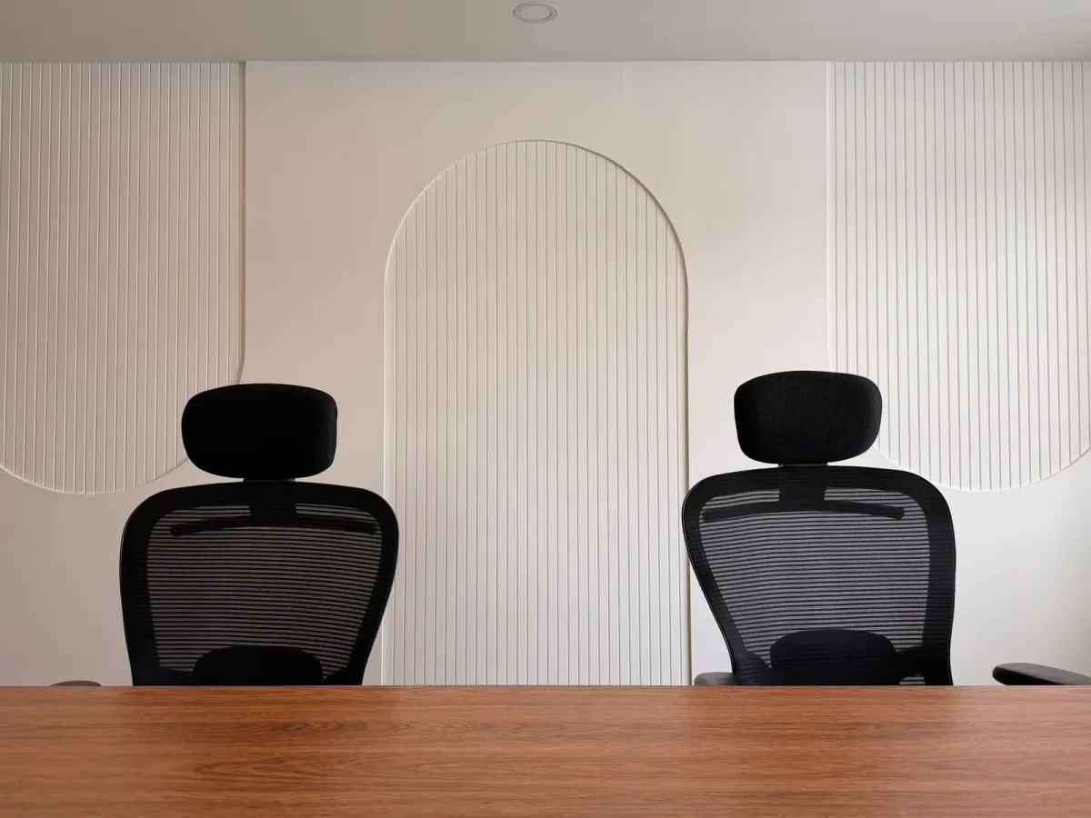 Two black office chairs behind a wooden desk, against a white panelled wall