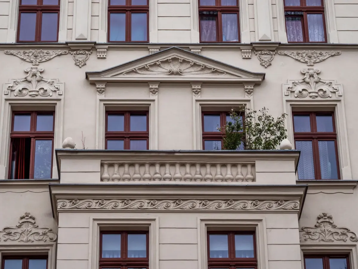Façade crème ornée de moulures, avec un balcon à balustres et des fenêtres en bois