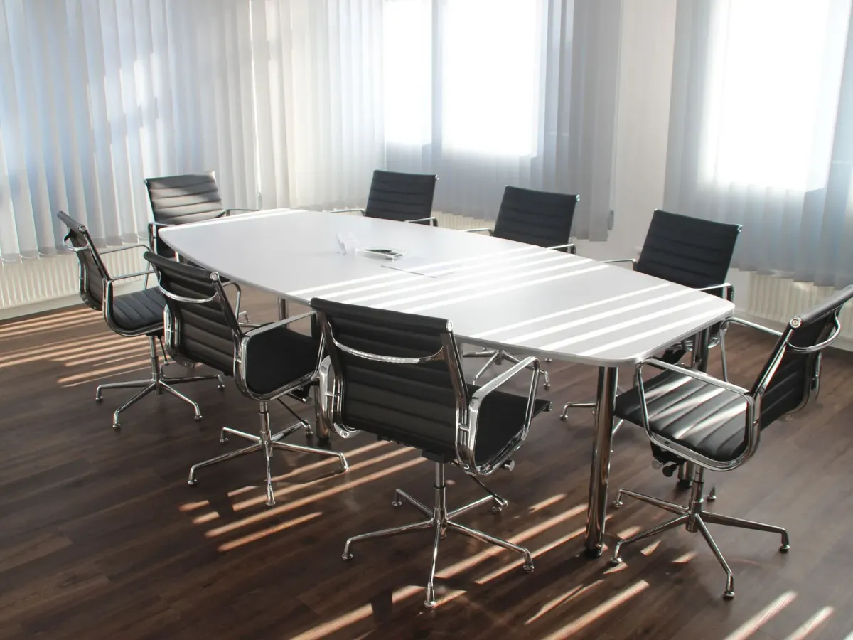 Salle de réunion ensoleillée, avec une table blanche entourée de fauteuils noirs