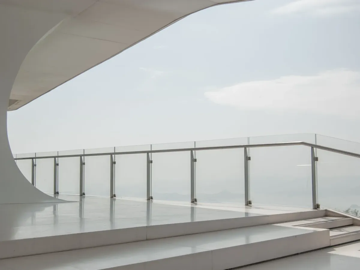 A white terrace edged by a glass railing, under a pale, hazy sky