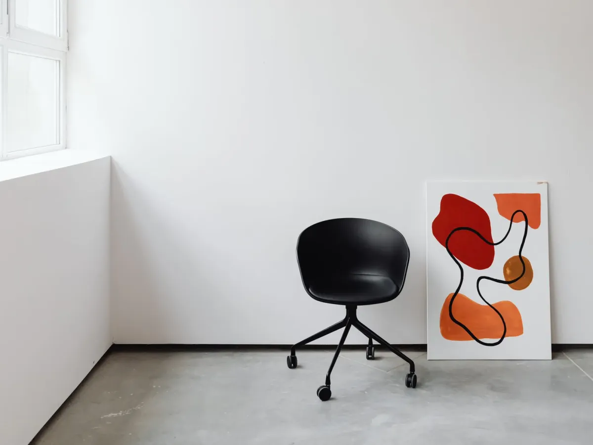 Œuvre abstraite posée contre un mur blanc, à côté d’une chaise noire