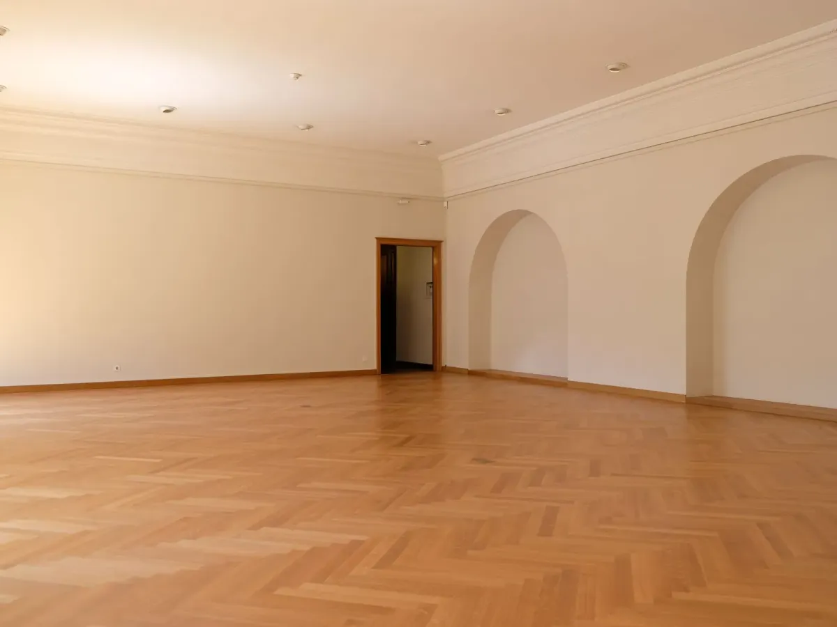 Grande pièce vide au parquet en chevrons, aux murs blancs et aux niches en arc