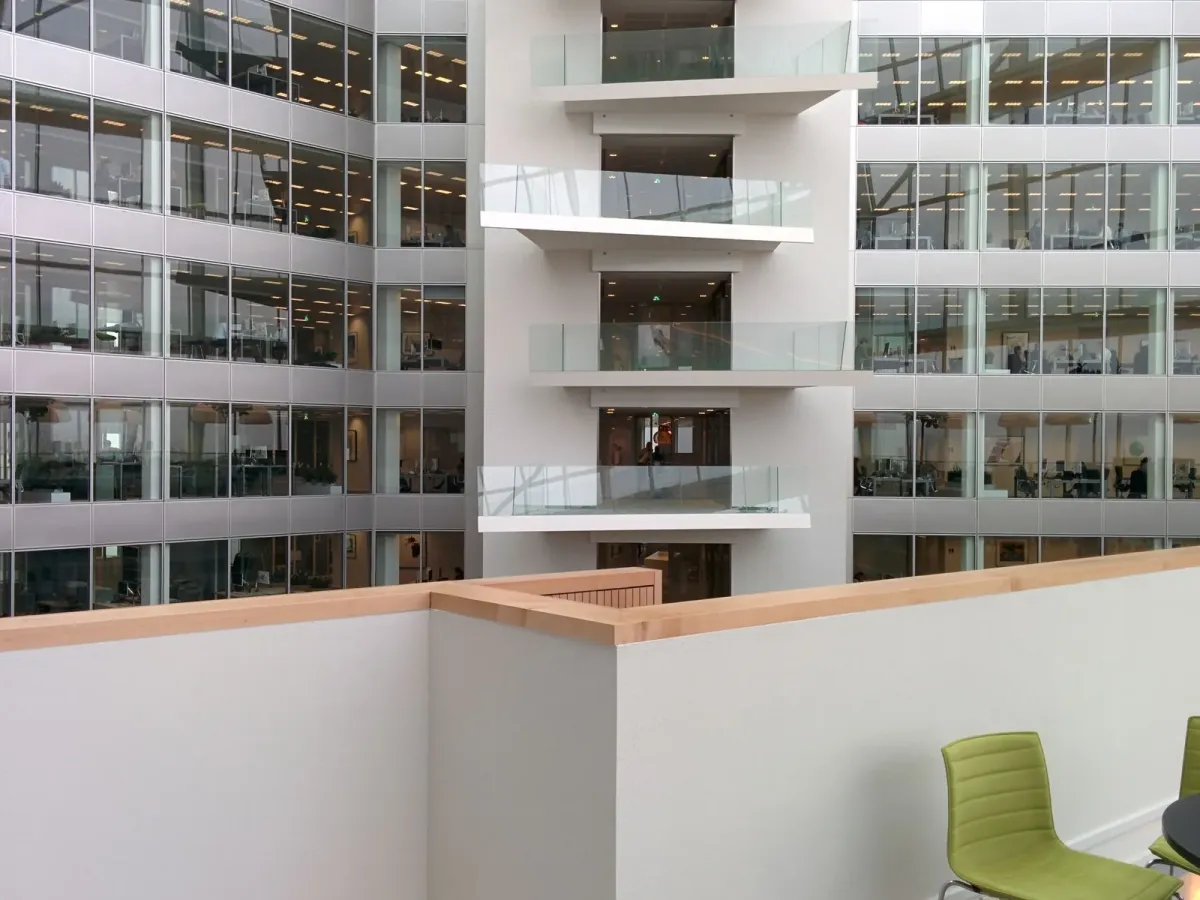 Atrium d’un immeuble de bureaux vitré sur plusieurs étages, avec des chaises vertes au premier plan