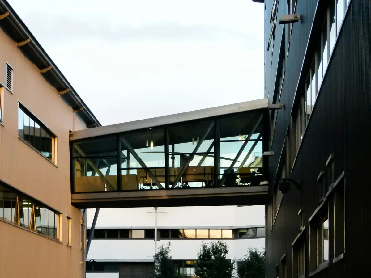 Glass-covered footbridge connecting two buildings with wooden and dark facades