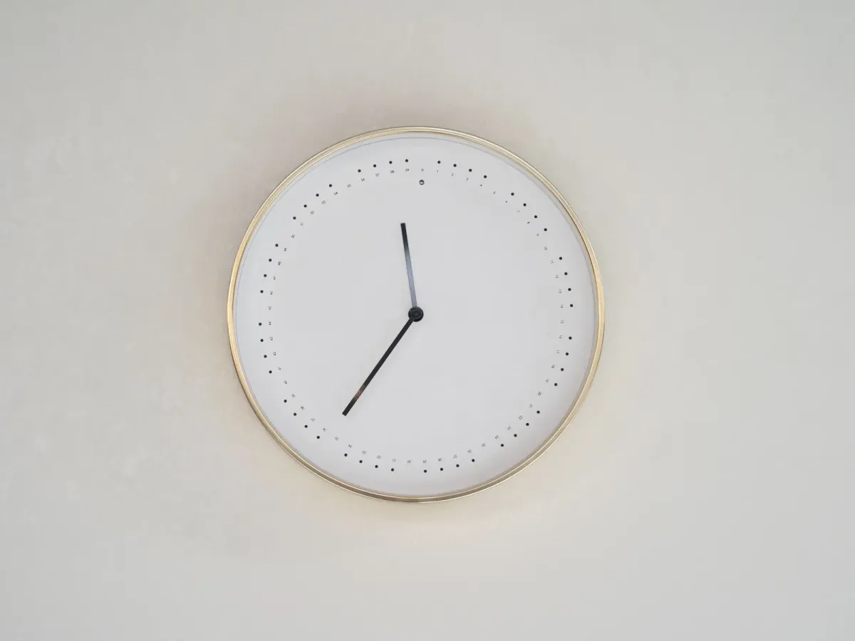 A minimalist wall clock with a thin gold rim on a pale wall