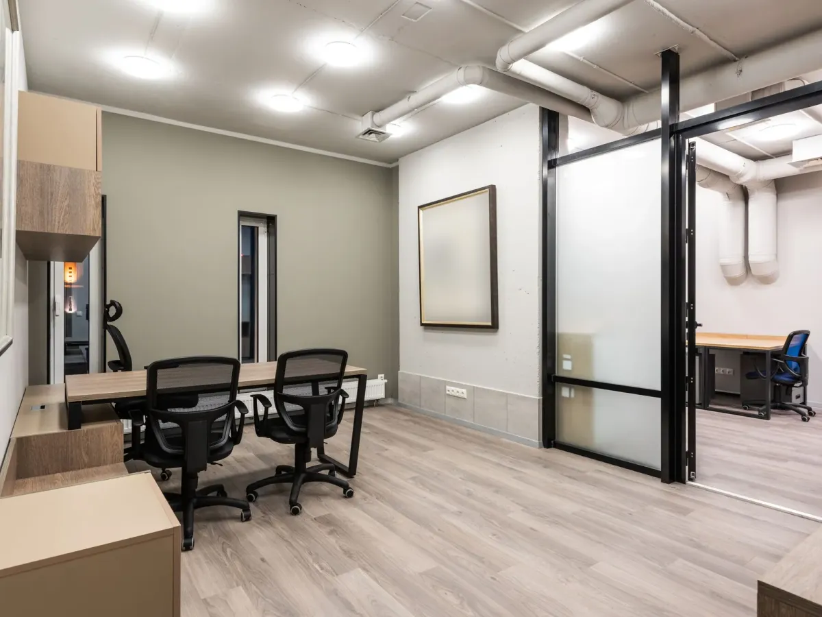 Bureau clair avec une table en bois et deux fauteuils noirs, près d’une porte vitrée
