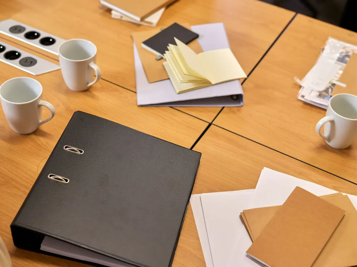 Binder, notebooks and coffee cups on a wooden meeting table, seen from above