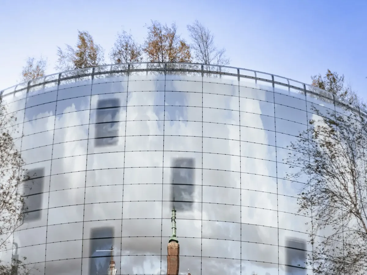 A curved mirrored facade reflecting clouds and bare trees