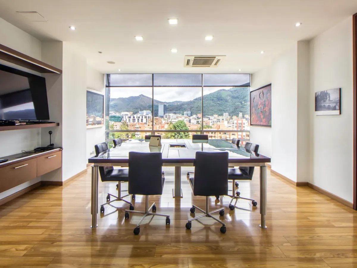 A boardroom with a glass table and black chairs facing a wide city view