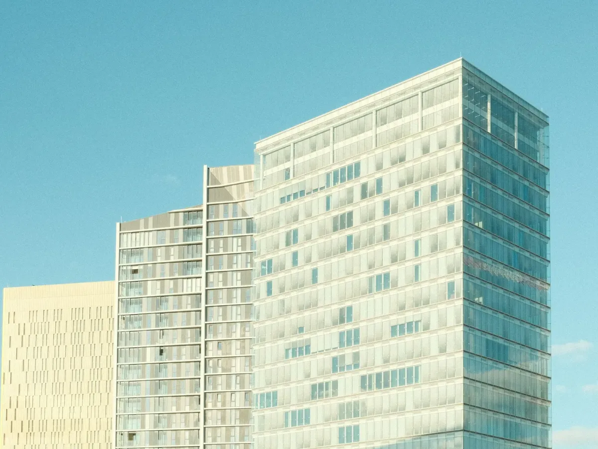 Two modern office buildings, one with vertical fins and one fully glazed, against a clear blue sky