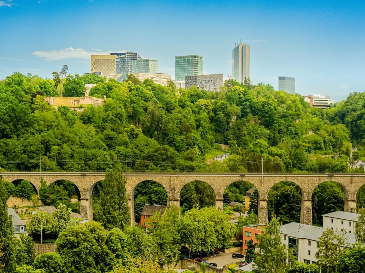 Viaduc en pierre dans la verdure de Luxembourg, avec les tours du Kirchberg à l’horizon