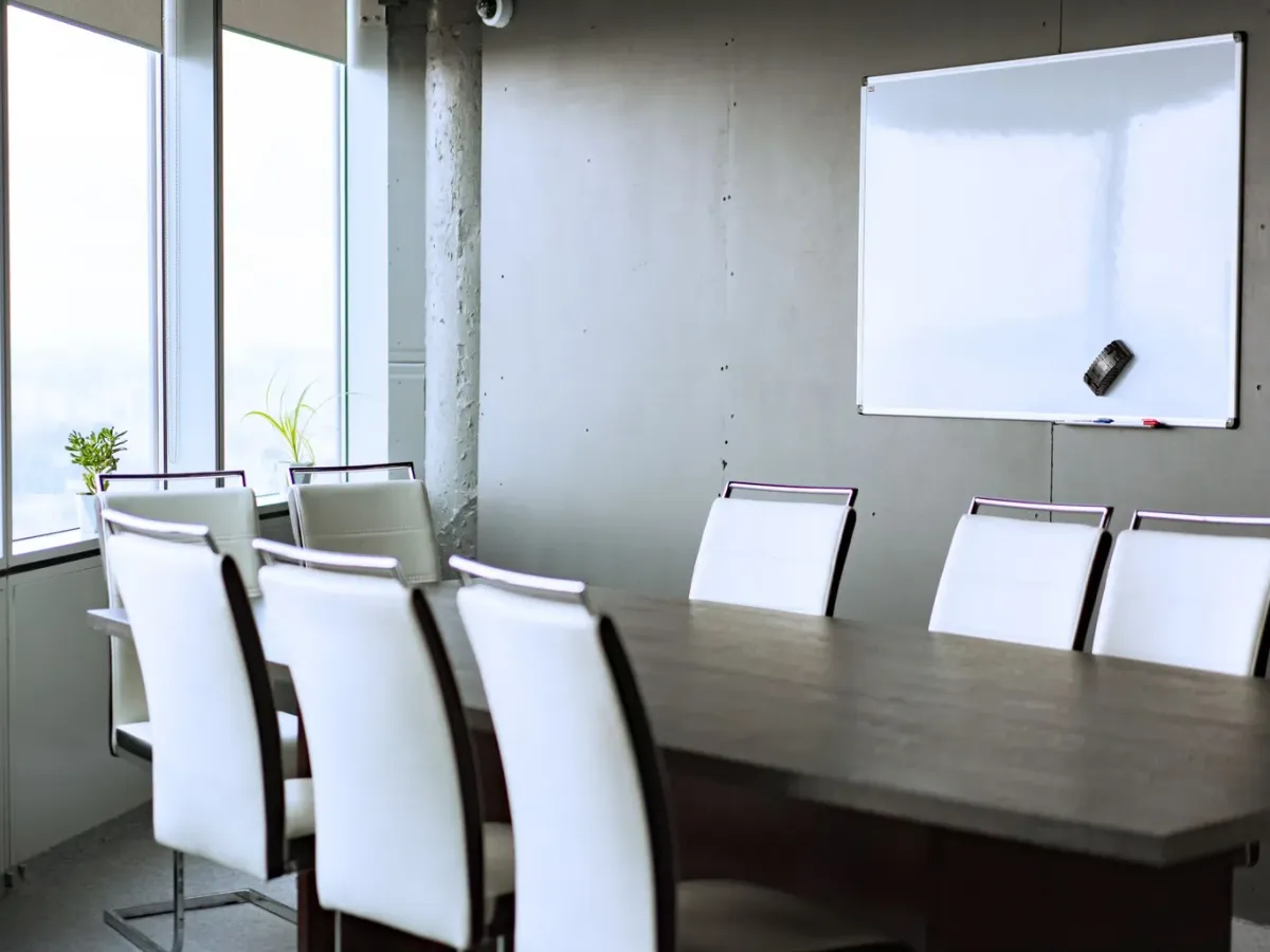 Bright meeting room with a long table, white chairs and a blank whiteboard
