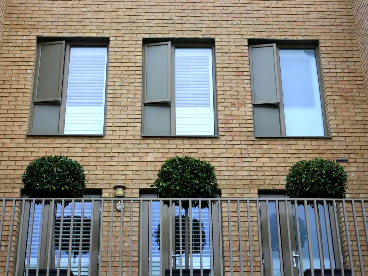 Façade de brique claire aux fenêtres régulières, au-dessus de buis taillés derrière une rambarde