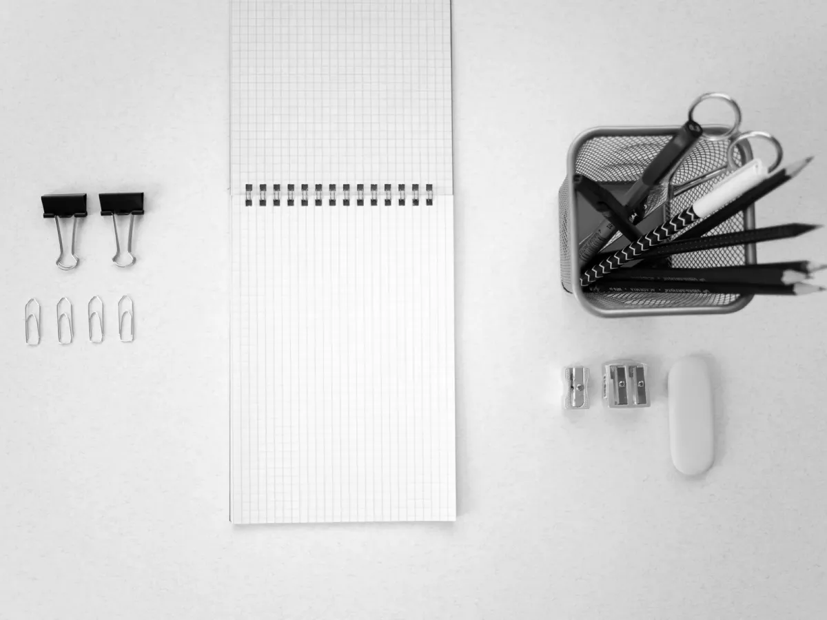 Pinces, trombones, bloc quadrillé et pot à crayons alignés sur un bureau blanc