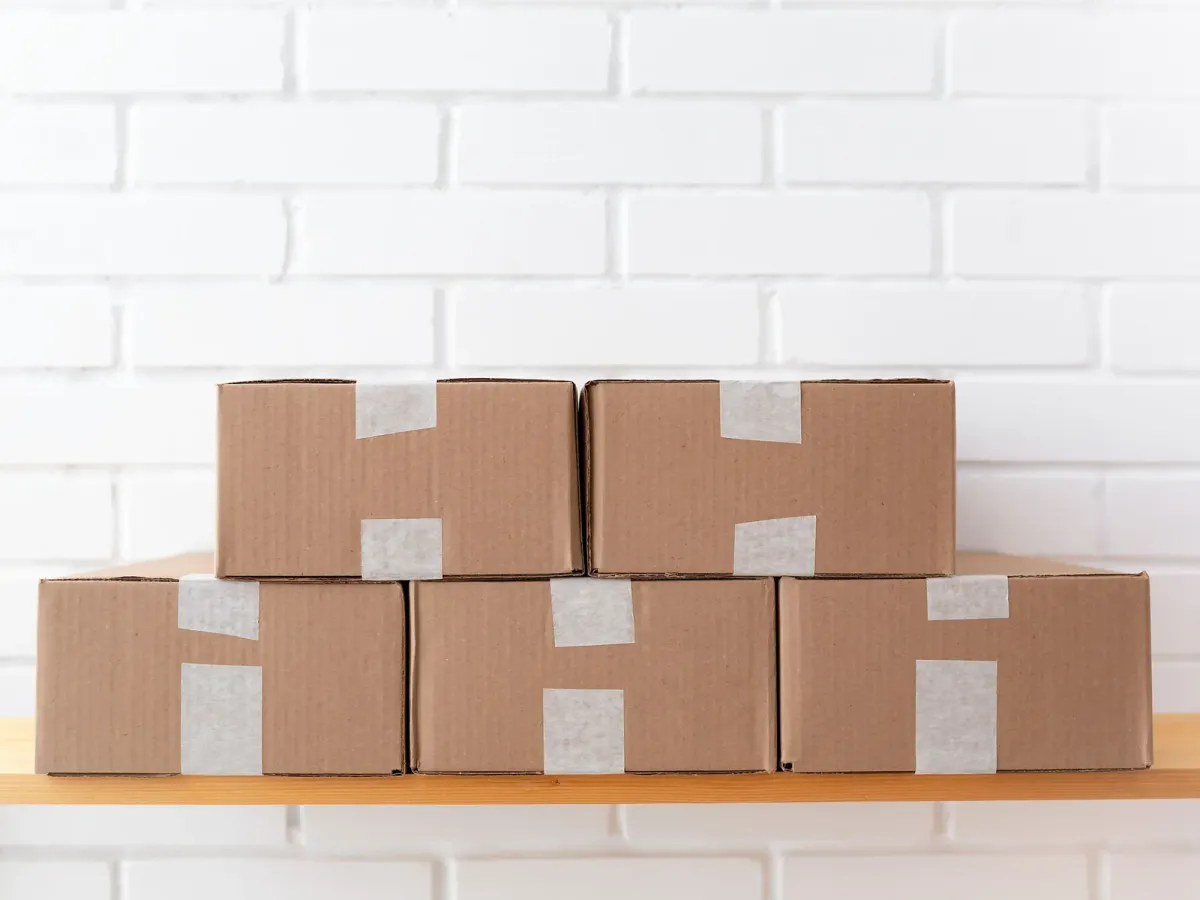 Cartons d’expédition empilés sur une étagère en bois, devant un mur de briques blanches